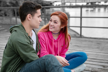 Music for two. Pretty young relaxed couple listening to music in earphones and looking relaxed while sitting on the pier