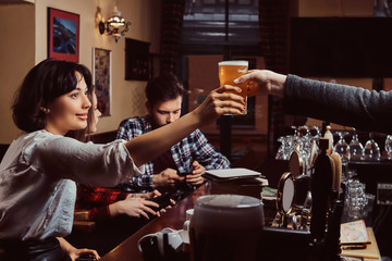 Young multiracial friends in bar. barman giving glass of beer to customer in pub.