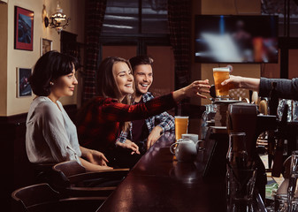 Young multiracial friends in bar. barman giving glass of beer to customer in pub.