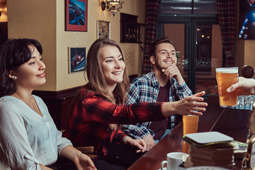 Young multiracial friends in bar. barman giving glass of beer to customer in pub.