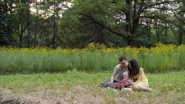 HD Family game. Mom and dad spend time reading a book to their little daughter in teh ground