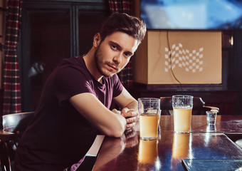 Young handsome man resting in the bar or pub, sitting with a glass of beer at wooden counter.