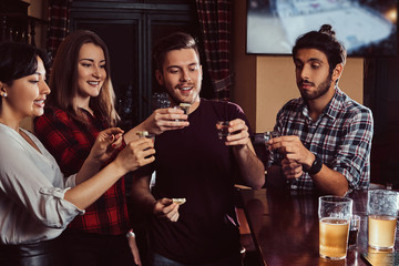 Group of happy multiracial friends making a toast with vodka while standing at bar or pub.