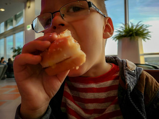 Caucasian boy blond with blue eyes eats sandwich and drinks lemonade through a straw. Rustic child...