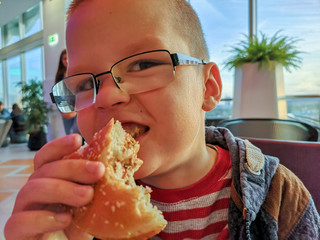 Caucasian boy blond with blue eyes eats sandwich and drinks lemonade through a straw. Rustic child...