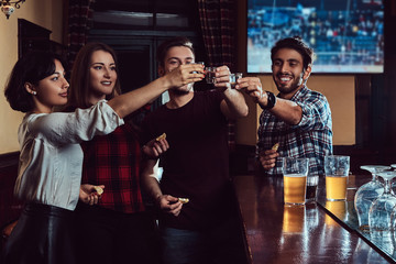 Group of happy multiracial friends making a toast with vodka while standing at bar or pub. - obrazy, fototapety, plakaty