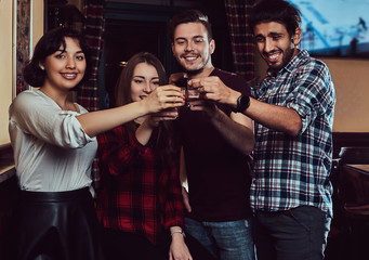 Group of happy multiracial friends making a toast with vodka while standing at bar or pub.