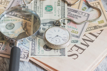 Pocket watch, American dollars and a magnifying glass