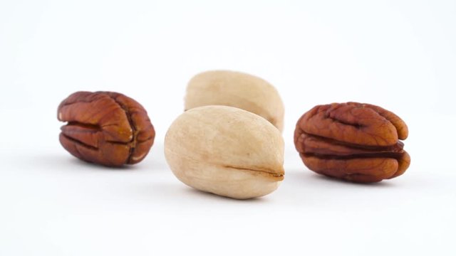 Two cracked pecan nuts and two kernels pecan nuts. Slowly rotating on the turntable isolated on the white background. Close up. Macro.