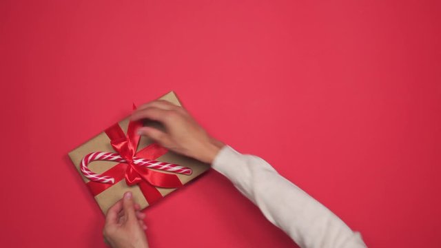 Hands placing Christmas gift box with lollipop on red flat lay