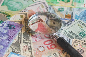 Different currency and magnifying glass, soft focus background