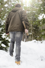 A man in a fashionable dress and yellow shoes with an ax in his hand going through the snowdrifts in the winter snow-covered forest, frosty day. Against the backdrop of green firs and pines.