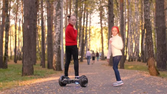 Preteen girls walking with gyroscooter on road in autumn park with sunlight