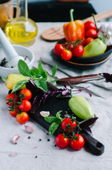 Cutting board surrounded by fresh raw tomato, sweet pepper, basil, olive oil and spice on the table