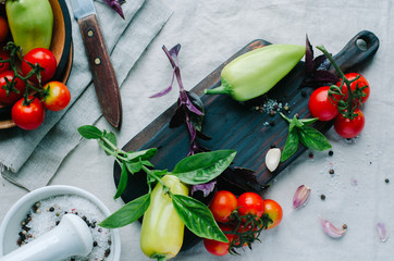 High angle still life view of cutting board surrounded by fresh raw vegetables and spices, basil on...
