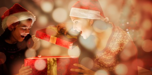 Composite image of festive mother and daughter opening a glowing