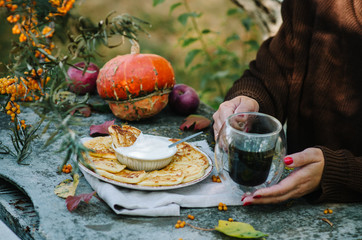 Autumn breakfast with pancakes. Cottage cheese pancakes кussian syrniki with sour cream. A woman in a brown sweater is drinking coffee.