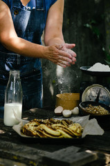 Cooking Cinnamon Roll Wreath. Women hands clapping and sprinkling white flour over dough. Ingredients on the table for the preparation of dough.