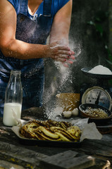 Cooking Cinnamon Roll Wreath. Women hands clapping and sprinkling white flour over dough. Ingredients on the table for the preparation of dough.