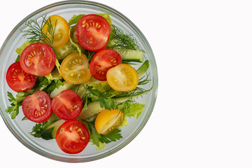 Salad of tomatoes, cucumbers, dill and parsley in a plate on a white background.