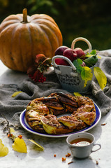 Freshly baked cinnamon sweet bun on rustic table. Cinnamon roll wreath at the autumn background whith pumpkin and a basket with apples.
