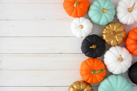 Autumn side border of various colorful pumpkins on a white wood background. Top view with copy space.