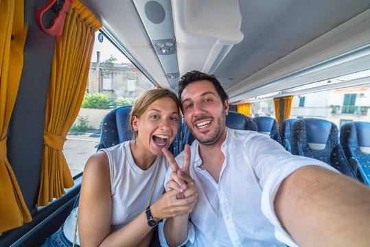 Backpackers traveling around the world on the bus. Young handsome man with his girlfriend on traditional bus taking selfie on smartphone.