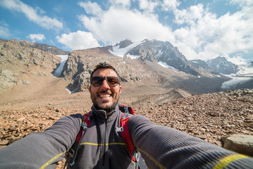 Self-portrait of a handsome young hiker in the top of the mountain with amazing landscape in background, kyrgyzstan, central asia