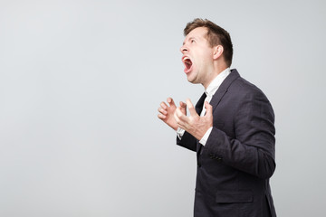 Side view of young caucasian man screaming loudly while standing isolated on gray background with...