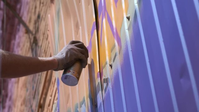 A young guy with a can of paint draws graffiti on the wall. One hand close-up