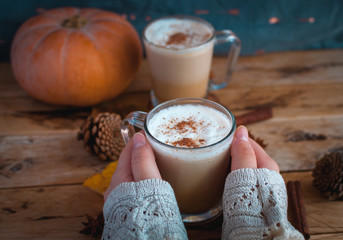 Close-up of hand holding pumpkin spice latte in glass cup on wooden background 