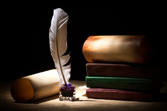 Literature concept. Old inkstand with feather near scrolls and books against black background. Dramatic light