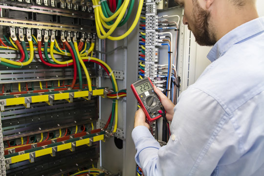 Electrician engineer testing cabling connection of high voltage power electric line in industrial distribution fuse board. Service man with multimeter. Tester in hands of electric worker.