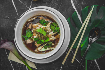 Asian soup with noodles in an iron plate on black stone table