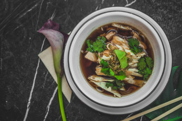 Asian soup with noodles in an iron plate on black stone table