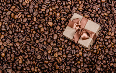 Gift box with ribbon on coffee background.  Roasted coffee beans background. Copy space