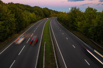 British dual carriageway road during sunset with rising full moon in the background - obrazy, fototapety, plakaty