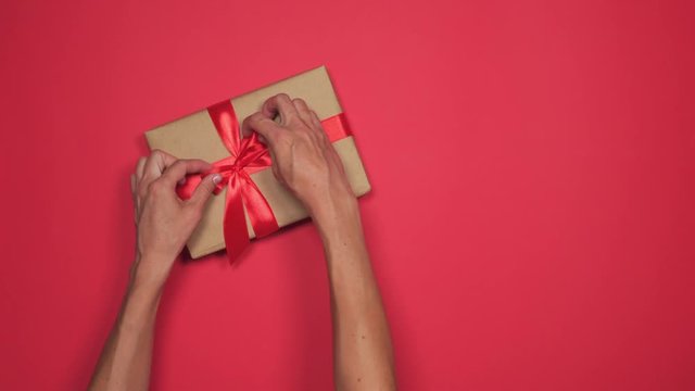 Hands presenting Christmas gift box on red flat lay