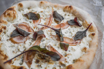 Delicious pizza with cheese and pear with leaves of green on the table in the restaurant
