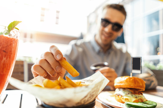 Close up of young attractive man eating french fries and burger at street cafe.