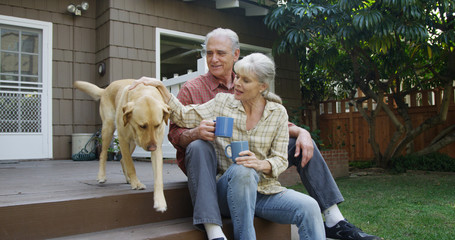 Senior couple having coffee petting dog in their yard - Powered by Adobe