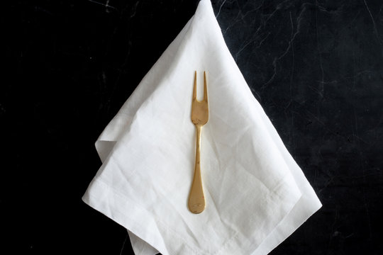 Gold fork on white linen against black marble.