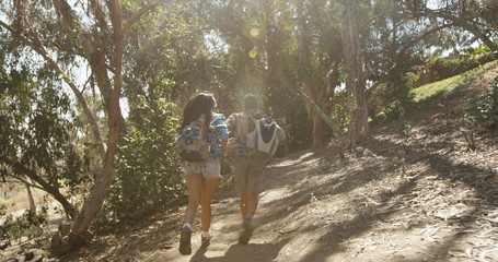 Young backpacker couple running through forest trees with golden light shining through trees