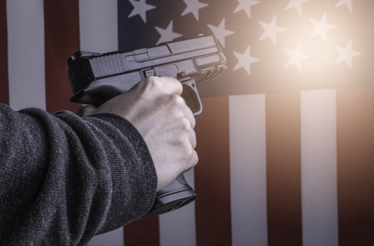 Woman's hand holding gun on flag of USA background. Gun Violence in the United States of America concept photo.