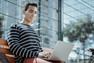 Without limits. Low angle of meditative male freelancer working on laptop and sitting on bench