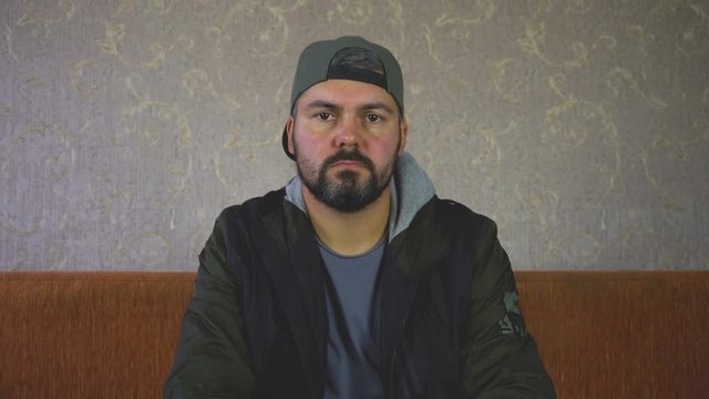 City dweller. Unshaven man. Moves to the beat of the music.. Sitting on the couch.On the wall light Wallpaper. Dark clothes. Close-up portrait. 4K video.