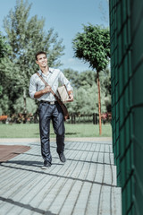 Express delivery. Low angle of pleasant male courier holding package and touching bag