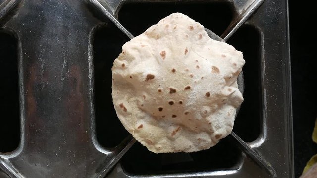 footage of making of Phulka a kind of Chapati: Indian thin bread made from wheat dough being baked on gas stove in home.