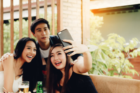 Group of asian friends sitting at bar restaurant and taking selfie