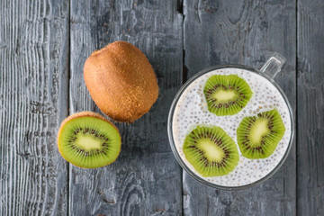 Kiwi fruit and a mug of black Chia seed pudding on a black wooden table. The view from the top. Flat lay.